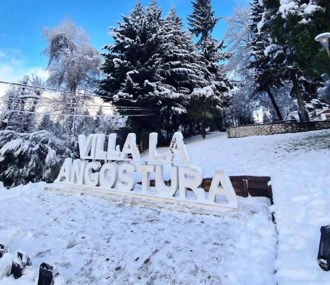 Cartel de Villa La Angostura bajo la nieve y cielo azul