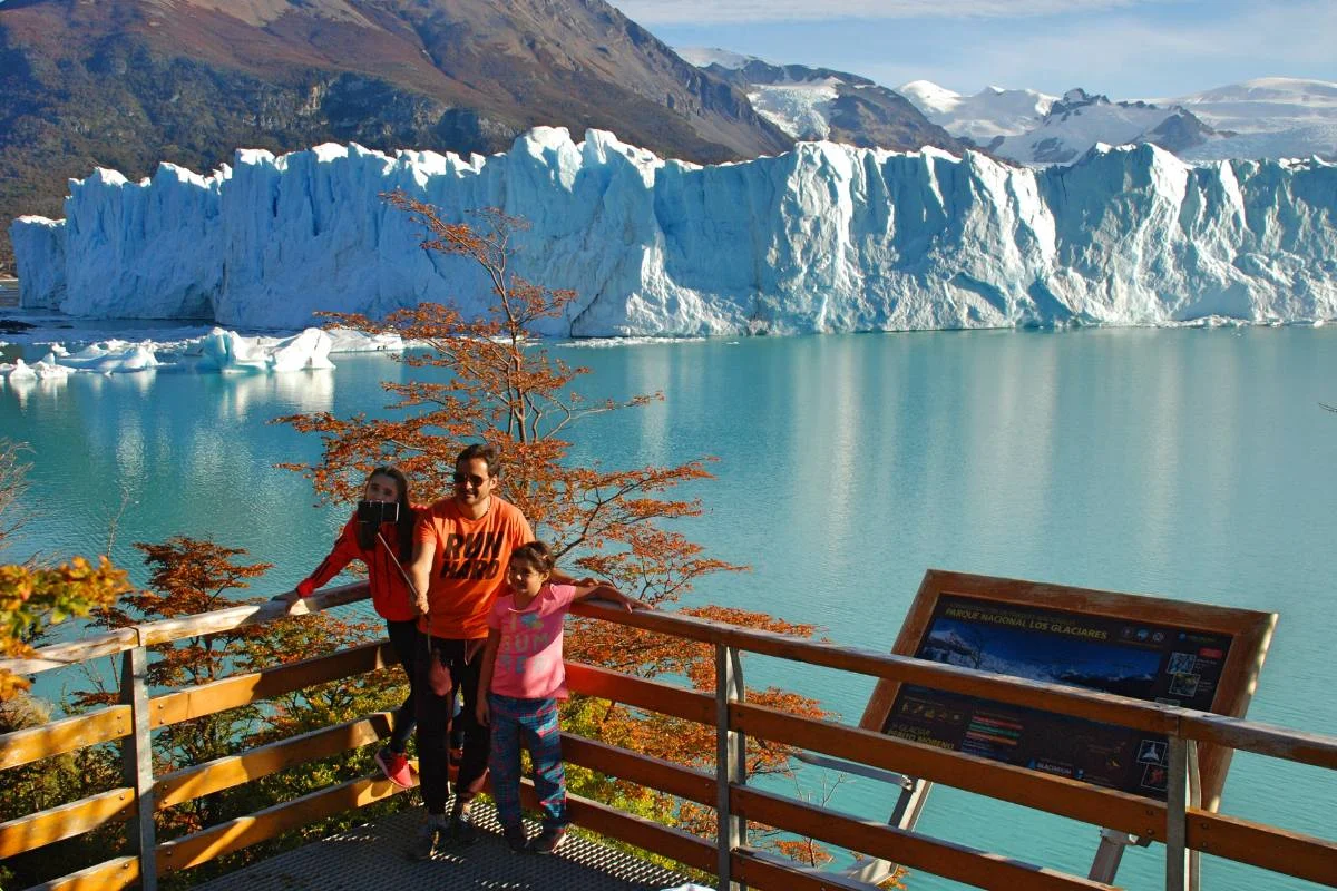 Familia en las pasarelas del Glaciar Perito Moreno en otoño — lenga roja en primer plano, el glaciar azul al fondo