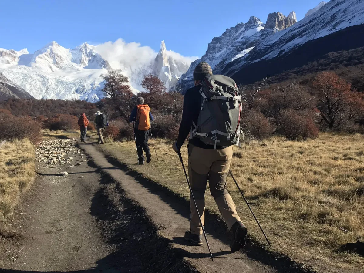 Trekkers caminando hacia el Cerro Torre por bosque de lengas otoñales en El Chaltén