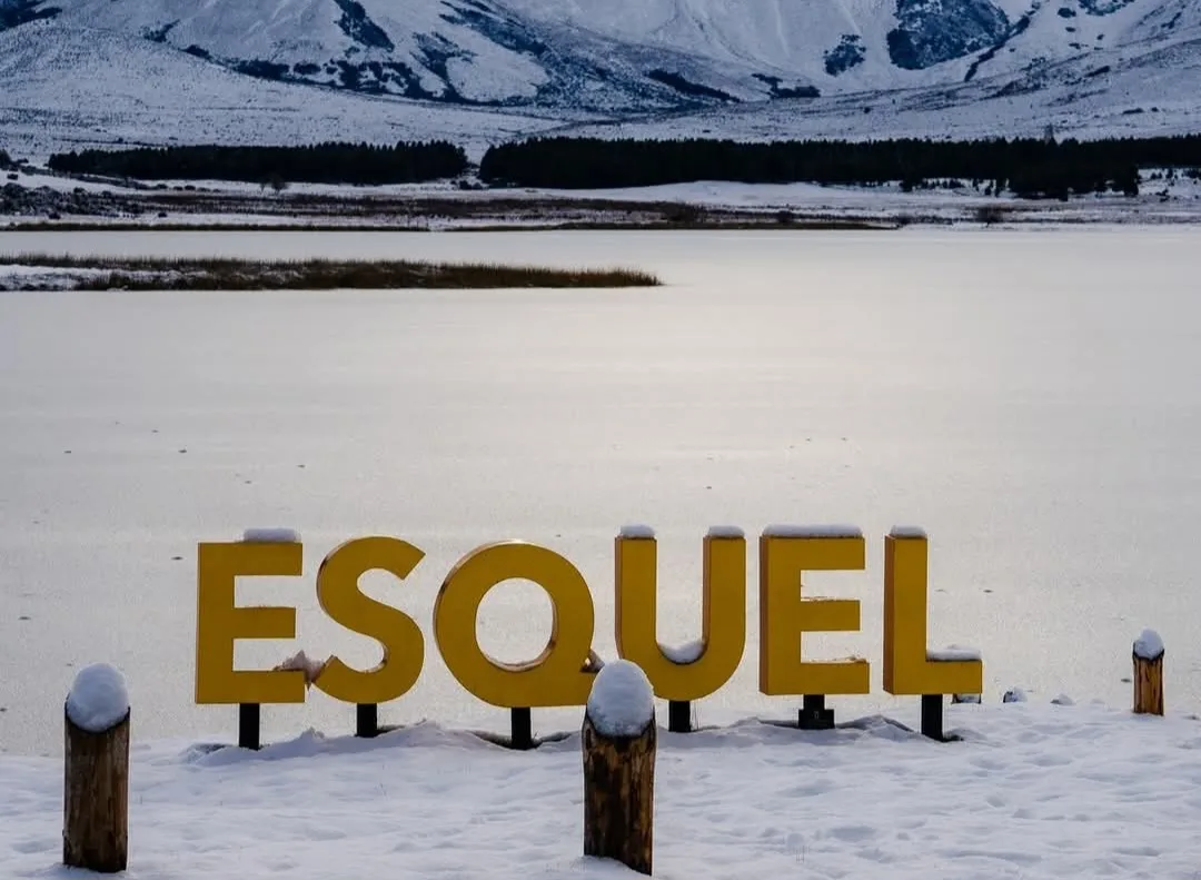 Cartel ESQUEL sobre el lago completamente helado y montañas nevadas de fondo