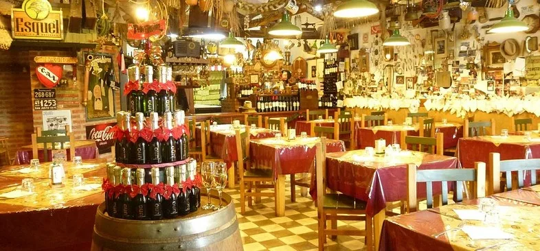 Interior de Don Chiquino — ambiente cálido con barrica, manteles a cuadros y decoración típica esquelense