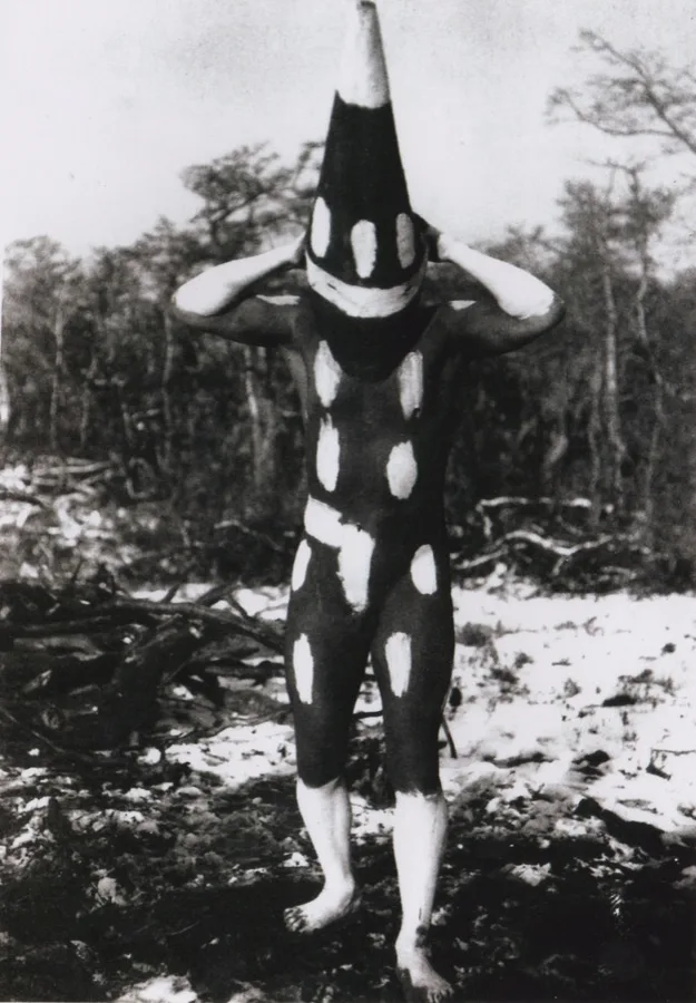 Figura selknam en la ceremonia del Hain — cuerpo pintado de negro con manchas blancas y máscara cónica, Tierra del Fuego c. 1923