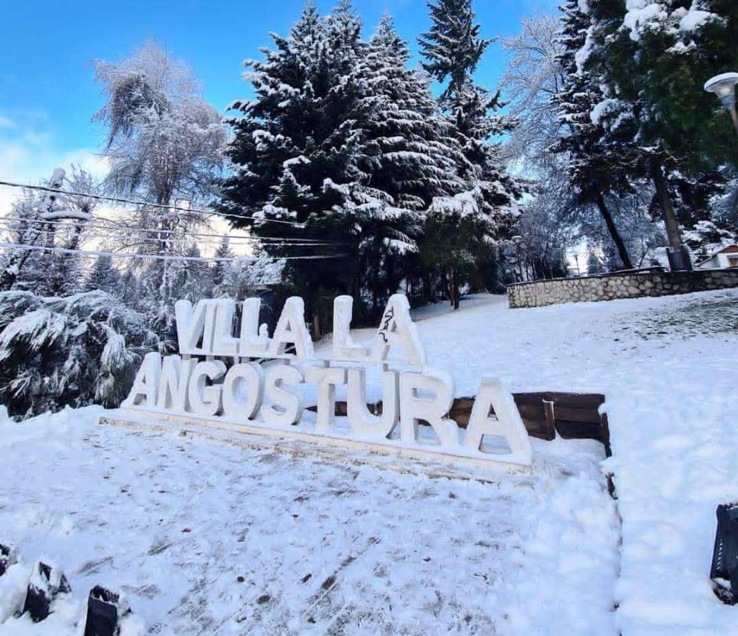 Cartel de Villa La Angostura bajo la nieve y cielo azul