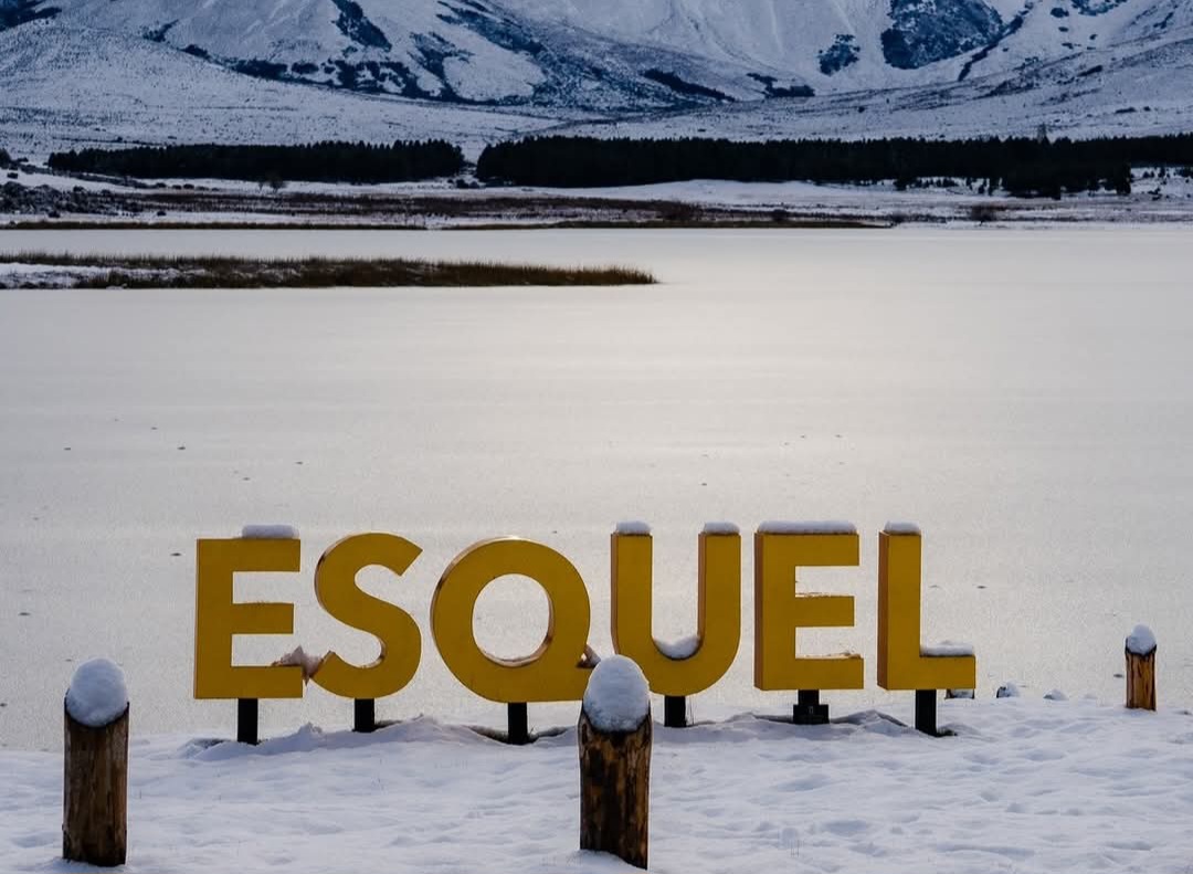 Cartel ESQUEL sobre el lago completamente helado y montañas nevadas de fondo
