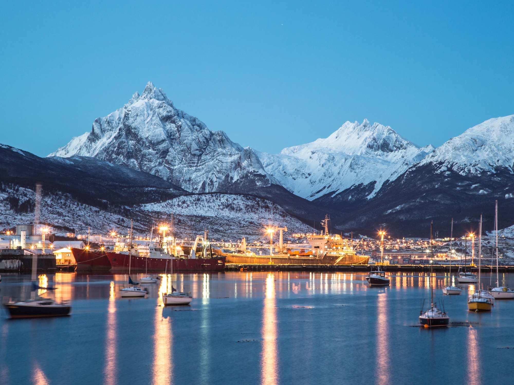 Puerto de Ushuaia en la hora azul — montañas nevadas y barcos reflejados en el Canal Beagle